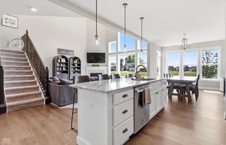 Modern open-concept kitchen and living room with white island, hardwood floors, large windows, and staircase