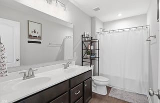 Modern bathroom with double sink vanity, large mirror, toilet, and white tile shower with glass enclosure