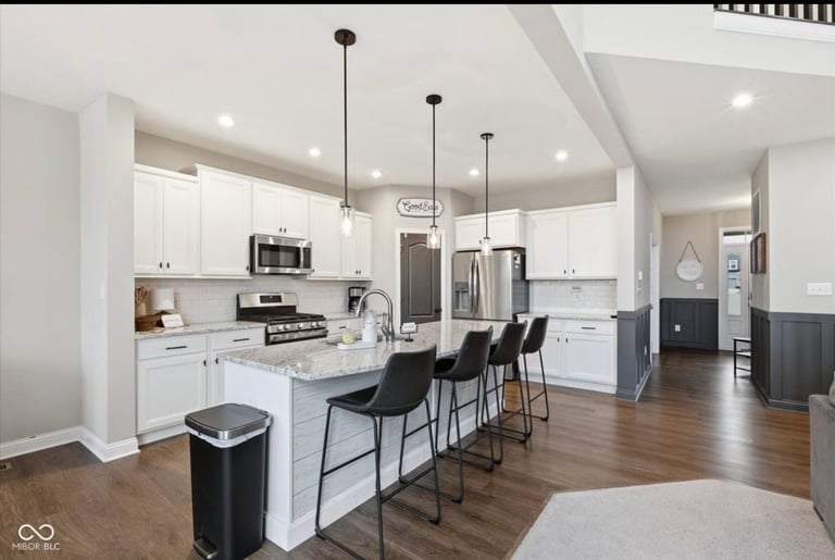 Modern kitchen with white cabinets, marble island with bar seating, stainless steel appliances, and pendant lighting