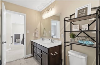Modern bathroom with dark wood vanity, white sink, mirror, and black metal shelving unit displaying decorative items and toiletries