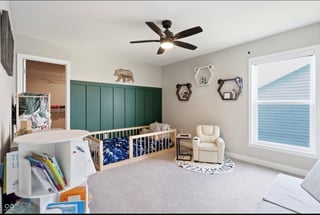 Modern nursery room with green headboard, white crib, cream armchair, ceiling fan, and animal-themed wall decor