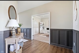 Modern entryway with gray wainscoting, wooden flooring, vanity with mirror and lamp, and open doorway to bright hallway