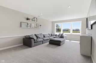 Modern living room with gray sectional sofa, floating shelves, large windows with countryside views, and light carpeting