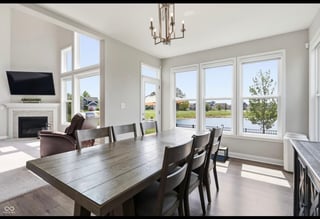 Modern dining room with wooden table, black chairs, fireplace, and large windows overlooking scenic landscape