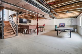Spacious industrial loft with wooden staircase, exposed ceiling beams, bar area with stools, and pool table in recreational space