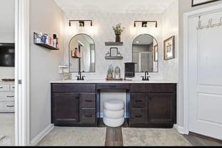 Modern bathroom with dual vanity, two arched mirrors, dark cabinetry, and white toilet on tile floor