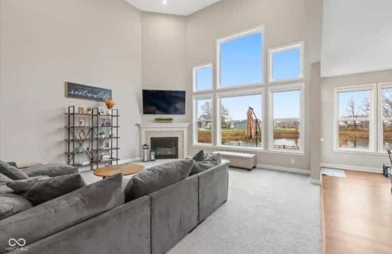 Modern living room with gray sectional sofa, fireplace, TV, and large windows overlooking landscape