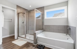 Modern bathroom with glass-enclosed shower, white soaking tub, gray tile walls, and wood flooring