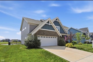 A modern two-story house with gray siding, white trim, and a two-car garage on a sunny day with manicured lawn and landscaping