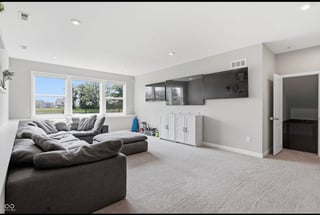 Modern basement recreation room with gray sectional sofa, entertainment center, and windows overlooking landscape