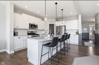 Modern kitchen with white cabinetry, stainless steel appliances, white quartz island with black bar stools, and wood flooring