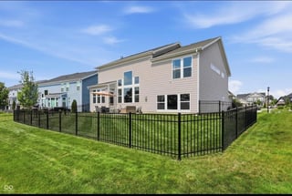 Modern two-story house with beige siding and black metal fence surrounding the backyard on a sunny day