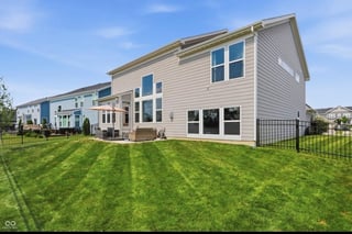 Modern two-story suburban house with beige siding, large windows, and manicured lawn with stripe pattern
