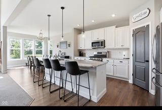 Modern open-concept kitchen with white cabinetry, island with seating, pendant lighting, stainless steel appliances, and hardwood floors
