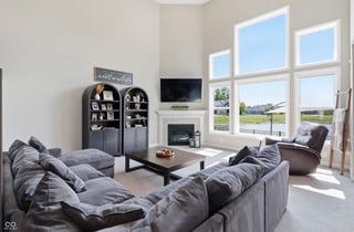 Modern living room with gray sectional sofa, fireplace, large windows overlooking landscape, and black storage shelves