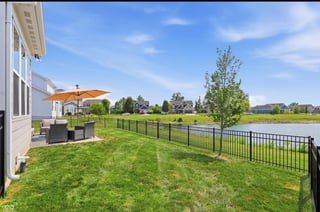 Backyard with orange umbrella, patio furniture, black fence, and manicured lawn overlooking open fields under blue sky